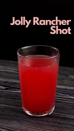 a glass filled with red liquid sitting on top of a wooden table