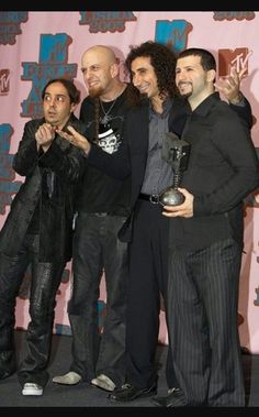 four men posing for the camera in front of a pink background