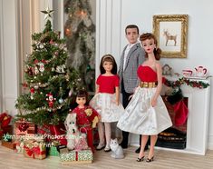 three dolls are posed in front of a christmas tree with presents on the floor next to it