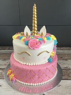 a cake decorated with pink, yellow and blue icing has a unicorn face on top