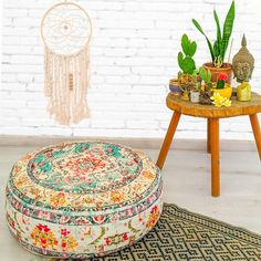 a round ottoman sitting on top of a rug next to a table with potted plants