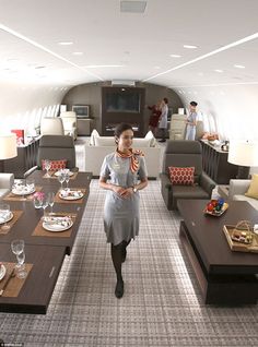 a woman is standing in the middle of an airplane dining area with tables and couches