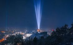 the light show is shining brightly in the night sky over a city with tall buildings and trees