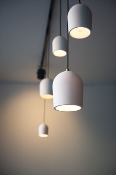 five white lamps hanging from a ceiling in a room with grey walls and flooring