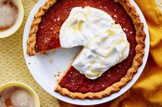 a piece of pie with whipped cream on top sits on a plate next to two cups