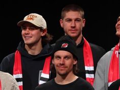 three men wearing scarfs and hats standing next to each other in front of a black background