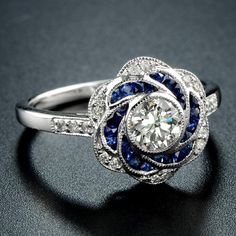 a diamond and blue sapphire flower ring on a black surface with the center stone surrounded by diamonds