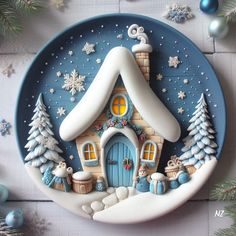 a blue plate with a house on it and snowflakes around the edge, surrounded by christmas decorations