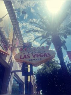 the las vegas sign is hanging from the side of a building with palm trees in front of it