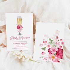 two cards with pink flowers on them next to a glass of champagne and a flower bouquet