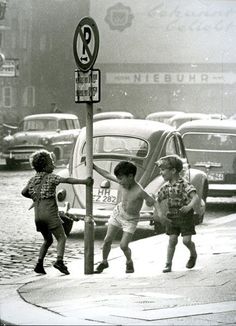 three children are playing on the sidewalk in front of cars and a no parking sign