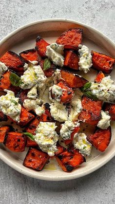 a white plate topped with sweet potatoes covered in feta cheese and minty herbs