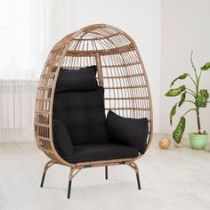 a rattan hanging chair with black cushions in a white living room, next to a potted plant