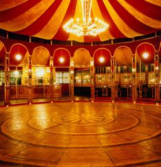 the inside of a circus tent lit up with chandeliers and lights in it