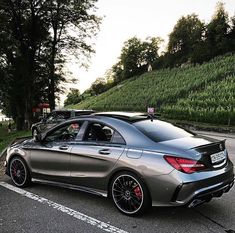 a silver car parked on the side of a road next to a lush green hillside