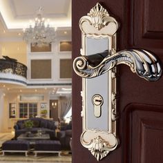 an ornate door handle on a brown wooden door in a large living room with chandelier