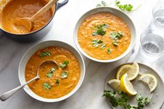 three bowls filled with soup and garnished with cilantro, parsley and lemon