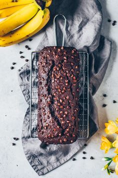 a loaf of chocolate cake sitting on top of a cooling rack next to some bananas