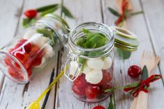 two mason jars filled with cherries and green leaves on top of a wooden table