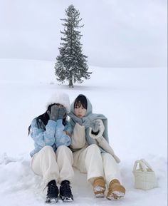 two people sitting in the snow next to a tree