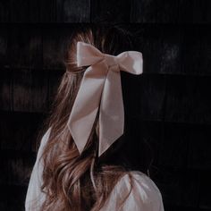 a woman with long brown hair wearing a large bow on her head, against a black background