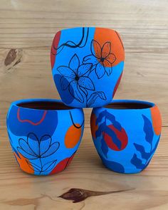 three colorful vases sitting on top of a wooden table with flowers painted on them