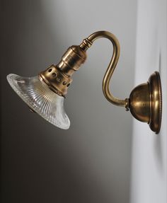 an antique brass wall light with a clear glass shade on it's arm, against a white wall