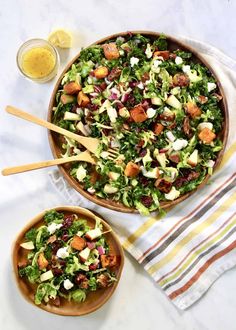 two wooden bowls filled with salad next to a glass of orange juice and spoons