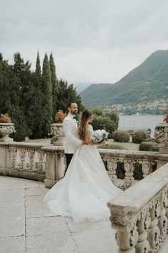 a bride and groom standing on a balcony looking at each other with mountains in the background