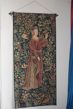 a tapestry hanging on the wall with a woman holding a bird in her right hand