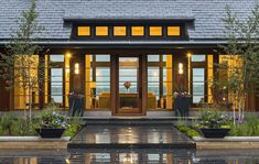 the front entrance of a house with potted plants and lights on it's windows