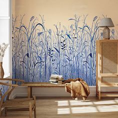 a living room with a wall painted with blue flowers and plants on the walls, next to a wooden bench