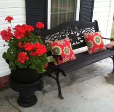 a black bench with red flowers and two pillows on it next to a potted plant