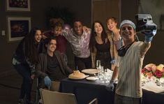 a group of people standing around a table with food and drinks in front of them