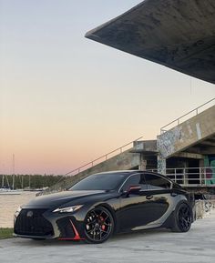 a black sports car parked in front of a large building near the water at sunset