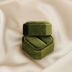 two green velvet boxes sitting on top of a white sheet