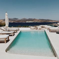 an empty swimming pool with chaise lounges and umbrellas on the beach next to it