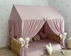 a child's bed with pink curtains and white teddy bears on the floor next to it