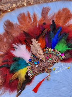 Oya inspired hand fan with 9 color feathers, brown ostrich feathers, mask mould, cowrie shells & jewels. Each item is respectfully made with the highest quality materials. Please note: All items are made to order and ship within 4-6 weeks! Style may slightly vary due to material availability. For custom color or style, you may ... Bohemian Headpieces For Carnival And Festivals, Bohemian Multicolor Headpieces For Carnival, Traditional Handmade Headpieces For Carnival, Traditional Handmade Carnival Headpieces, Djembe Drum, Cowrie Shells, Ostrich Feathers, Cowrie Shell, Hand Fan