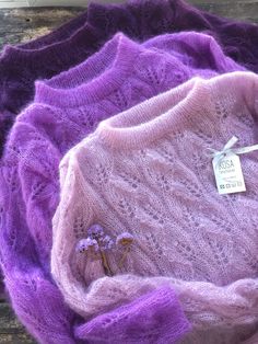 a purple knitted sweater sitting on top of a wooden table next to a tag