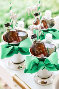 three bottles of liquor are sitting in silver cups with green bows on the top and one bottle is empty