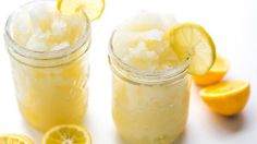 two mason jars filled with lemonade and ice next to sliced lemons on a white surface