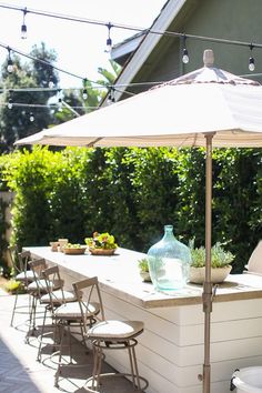 an outdoor table with chairs, umbrella and potted plants on the counter in front of it