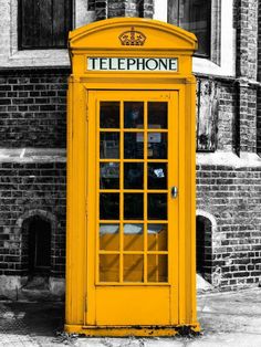 a yellow telephone booth sitting in front of a brick building