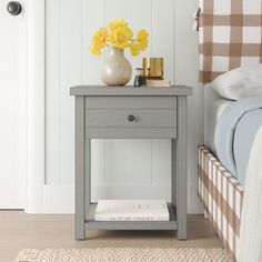 a nightstand with yellow flowers on it next to a bed and white walls in a bedroom