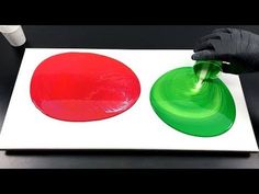 a person in black gloves is painting two red and green circles on a white board