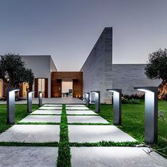 a modern house with grass in the front yard and walkway leading to it at night