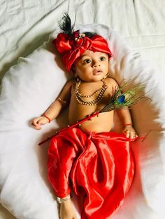 a baby wearing a red dress and headband laying on top of a white blanket