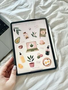 a person's hand holding an ipad next to a laptop on a bed with white sheets