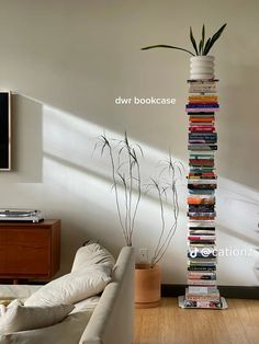 a tall stack of books sitting on top of a wooden floor next to a white couch